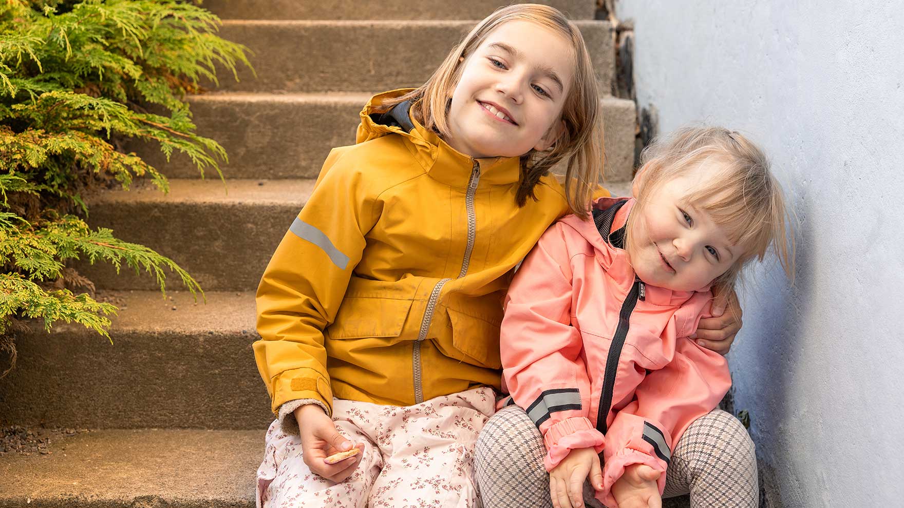 Two girls are sitting side by side on the stone steps, smiling.