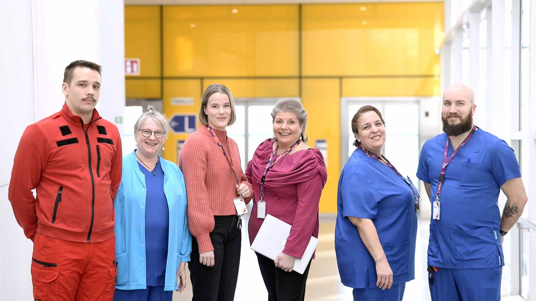 Six employees are standing side by side, looking at the camera.