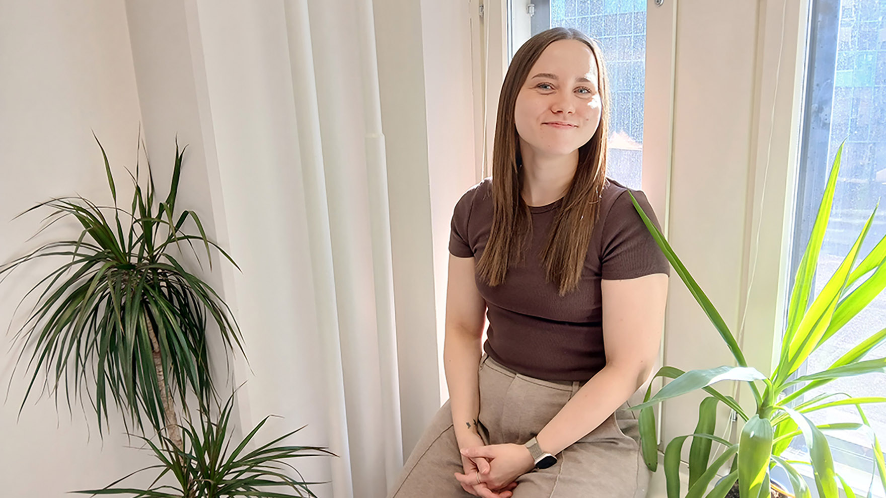 Nainen istuu ikkunalaudalla hymyillen.