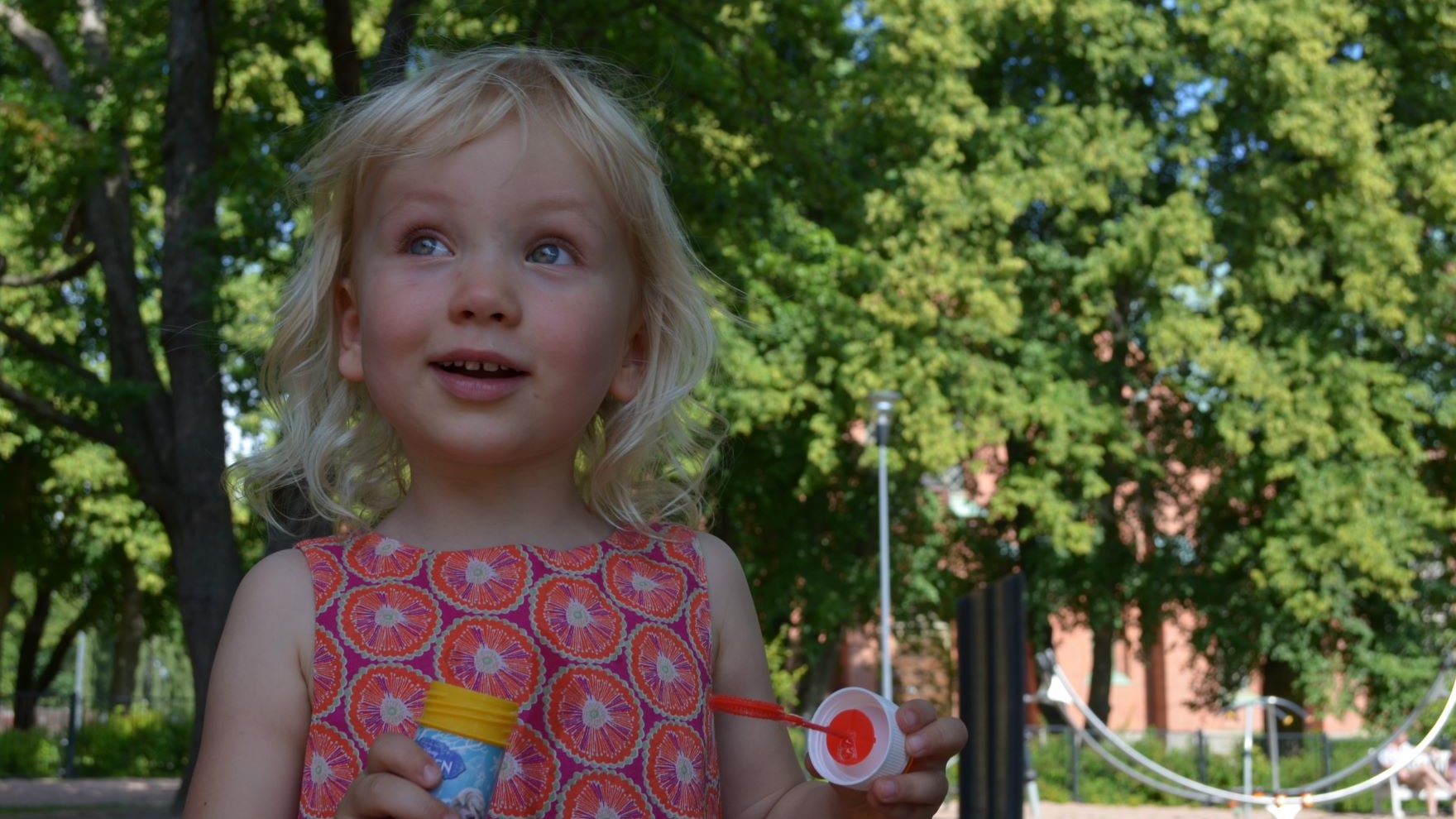 Tyttö hymyilee puistossa ja kädessään on saippuakuplapullo.