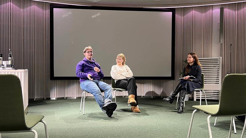 Kolme ihmistä istuu tuoleilla kokoustilan etuosassa.