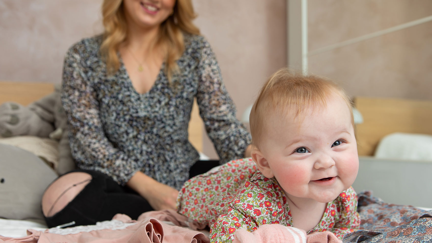 A baby is smiling with the mother in the background.