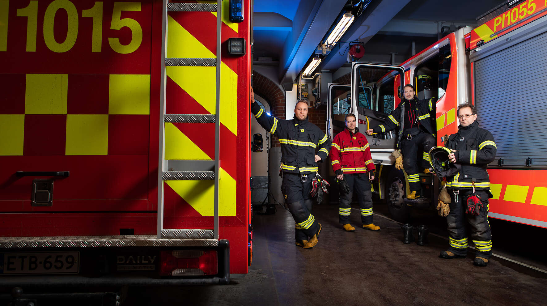 Paloasemalla kahden paloauton vieressä poseeraa neljä pelastajaa työasuissaan.