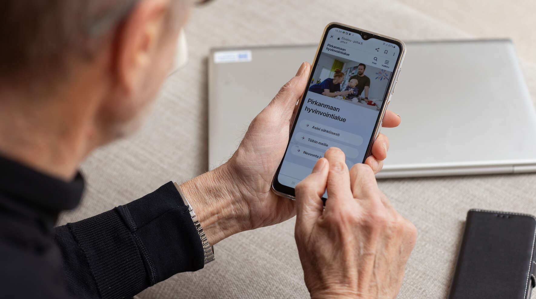 Henkilö selaa puhelimella hyvinvointialueen nettisivuja.