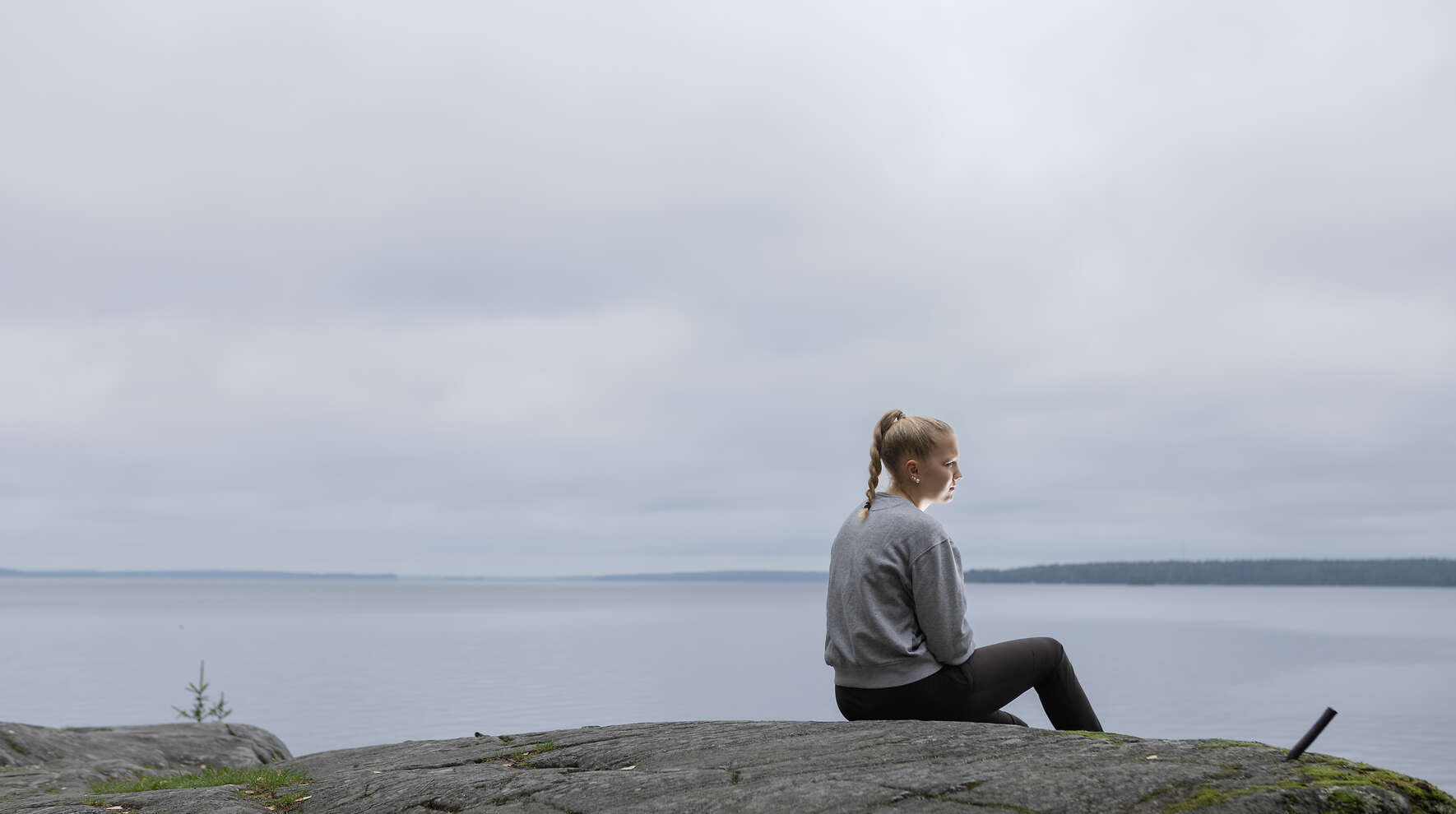 Henkilö istuu kalliolla järven rannassa.