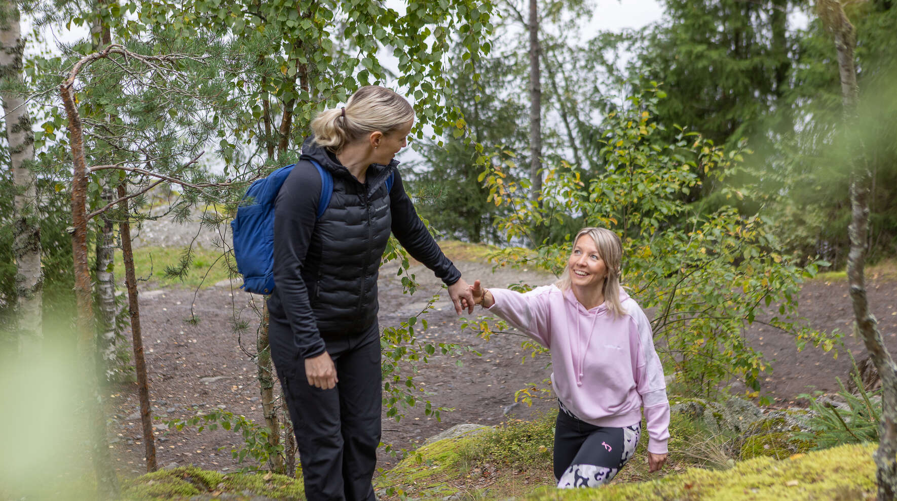 Kaksi henkilöä nousee kalliota ja toinen auttaa toista kädestä.