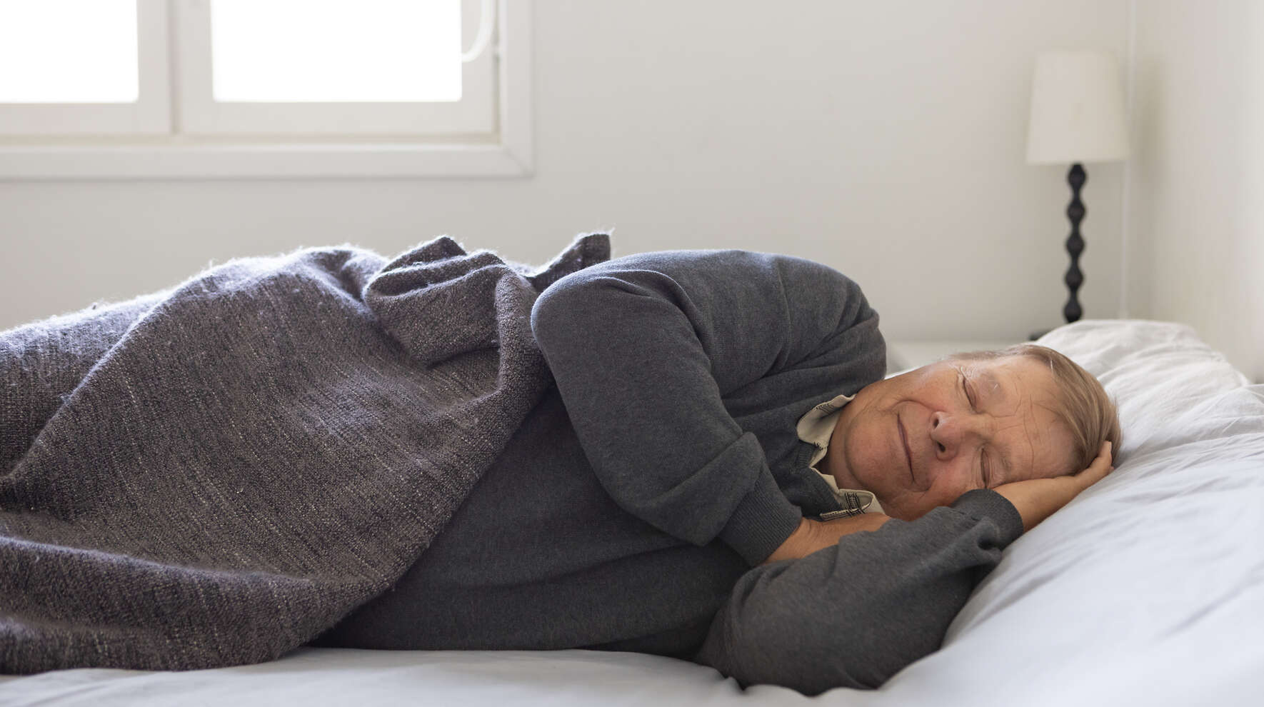 Mies nukkuu vuoteessa päiväunilla viltin alla.