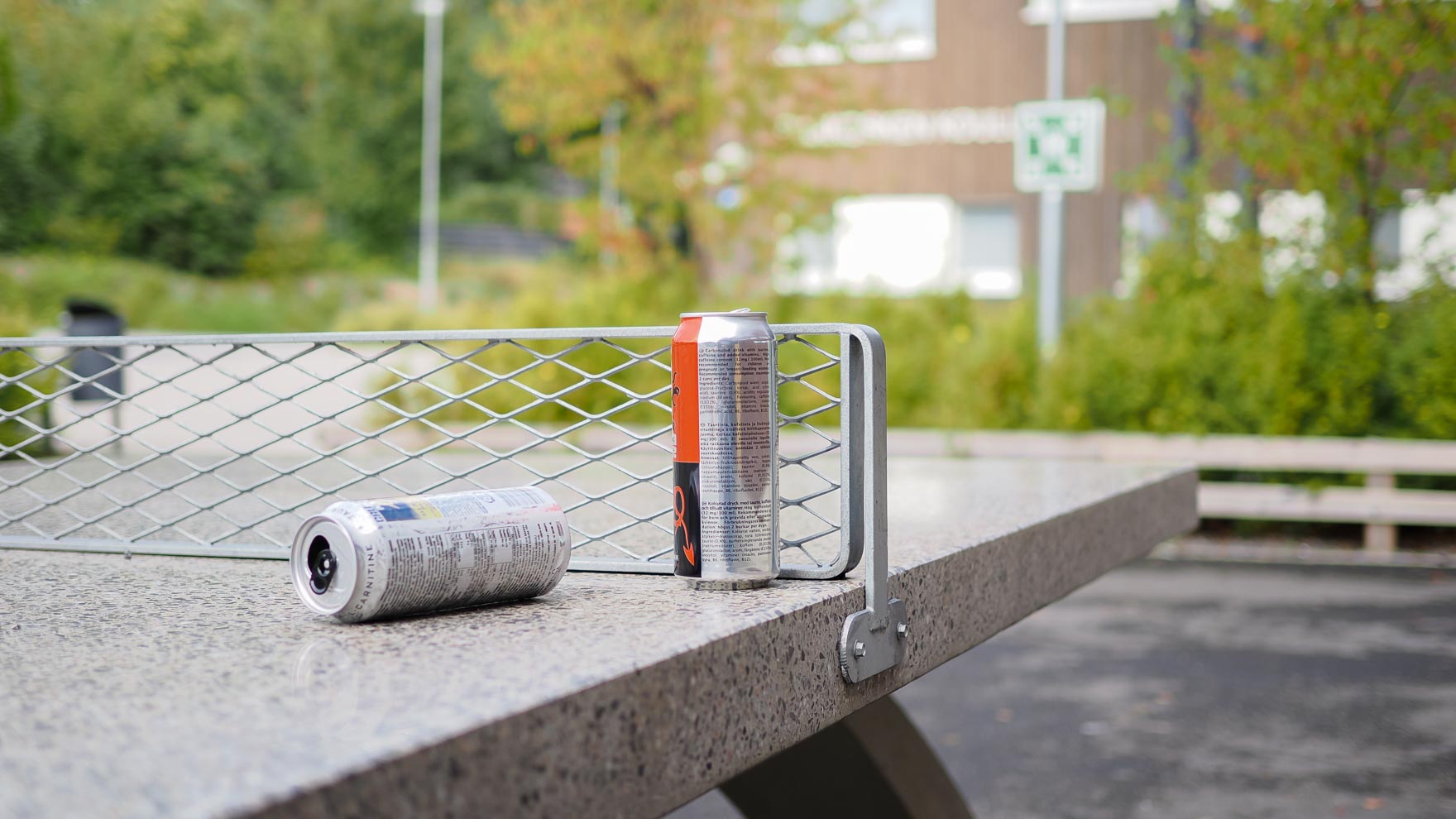 Kaksi energiajuomatölkkiä koulun pihalla olevan pingispöydän päällä.