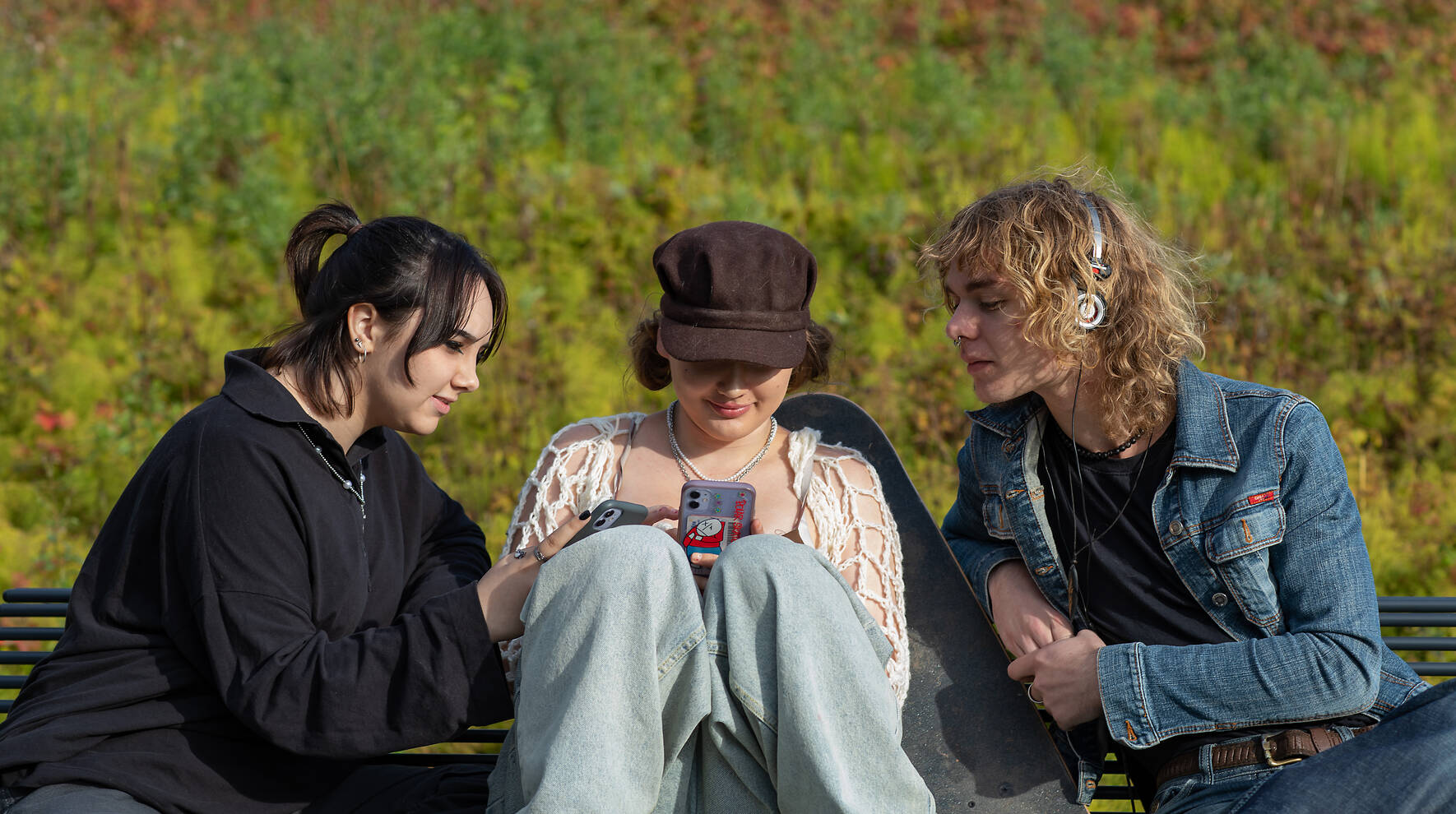 Kolme nuorta istuvat puistonpenkillä ja katsovat älypuhelimien näyttöjä.