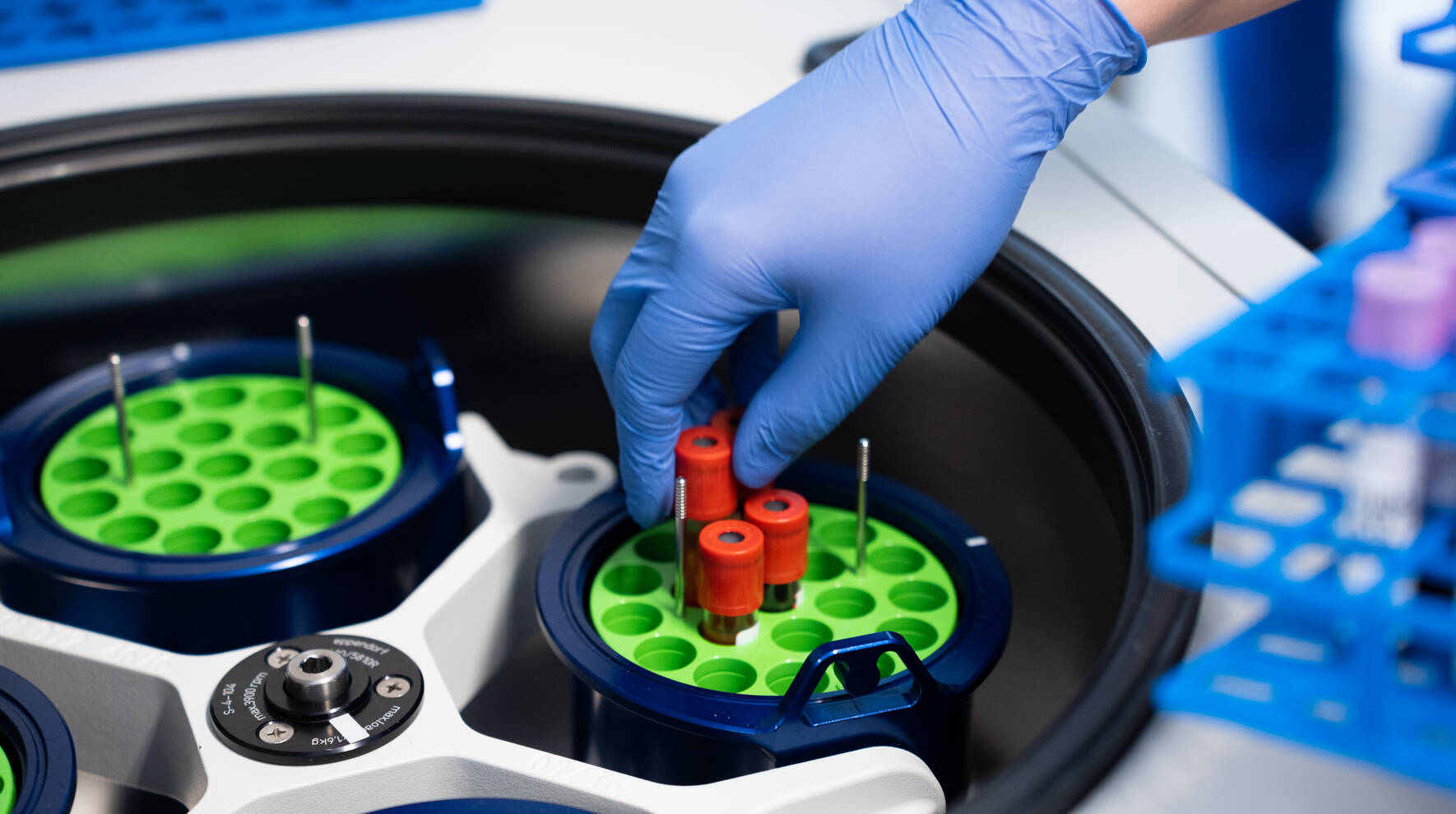 Kuvassa on näytteitä erottelulaitteessa sekä hansikkaalla suojattu käsi, joka asettelee putkiloita paikoilleen.