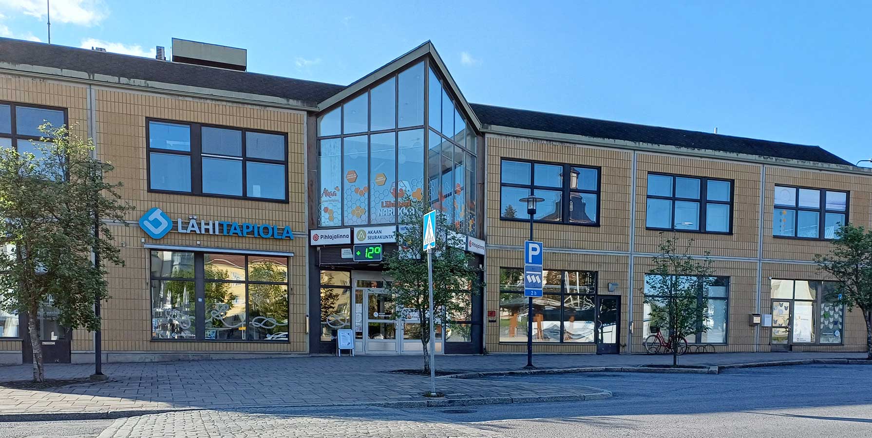 Keltatiilisen rakennuksen korkeahko lasinen sisäänkäynti.