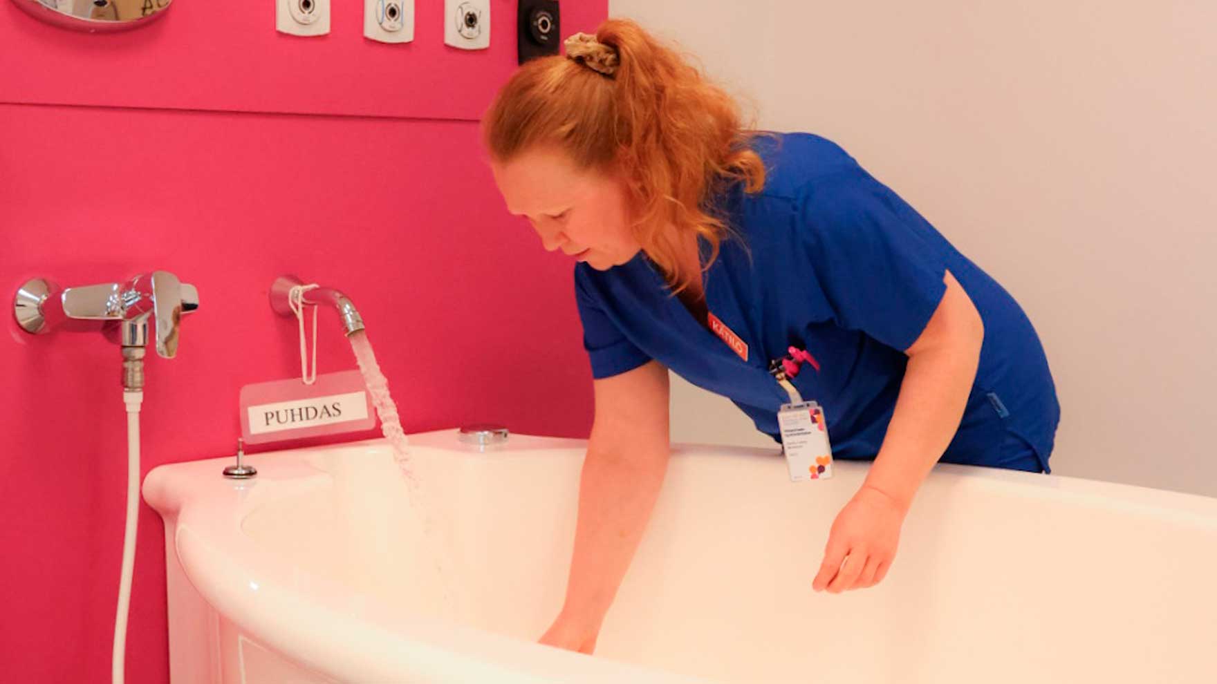 Kätilö seisoo ammeen äärellä ja laskee siihen vettä.