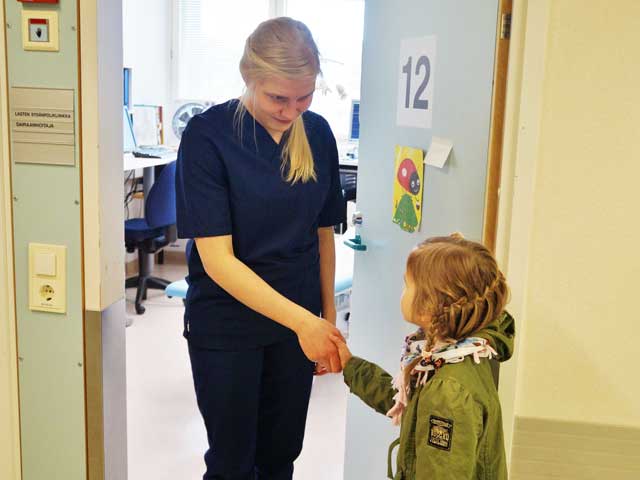 Hoitaja kättelee tyttöä tutkimushuoneen ovella.