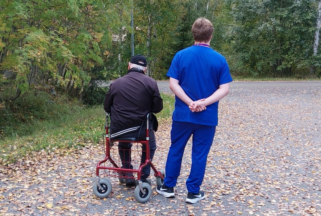 Rollaattorissa istuva ikäihminen ja Pirhan työntekijä ovat ulkona.