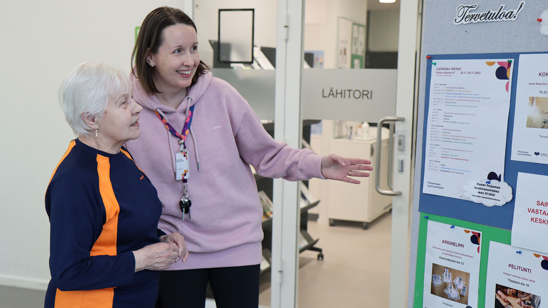 Ikääntynyt ja työntekijä katsovat lähitorin ilmoitustaulua.
