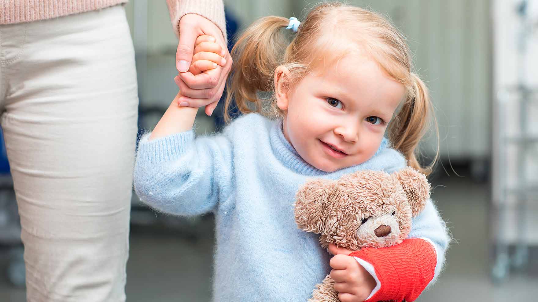 Lapsipotilas nalle sylissä ja käsi aikuisen kädessä.