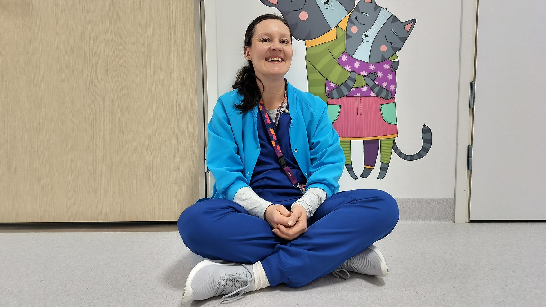 Marinka istuu hymyillen hallinnon osaston lattialla. 