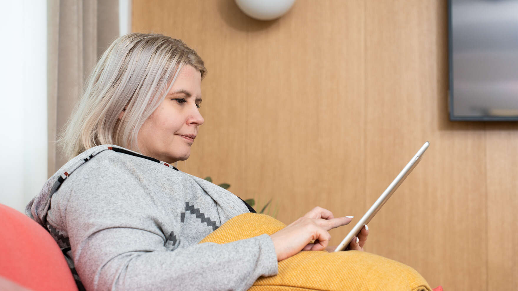 Nainen istuu ja selailee tablettia.