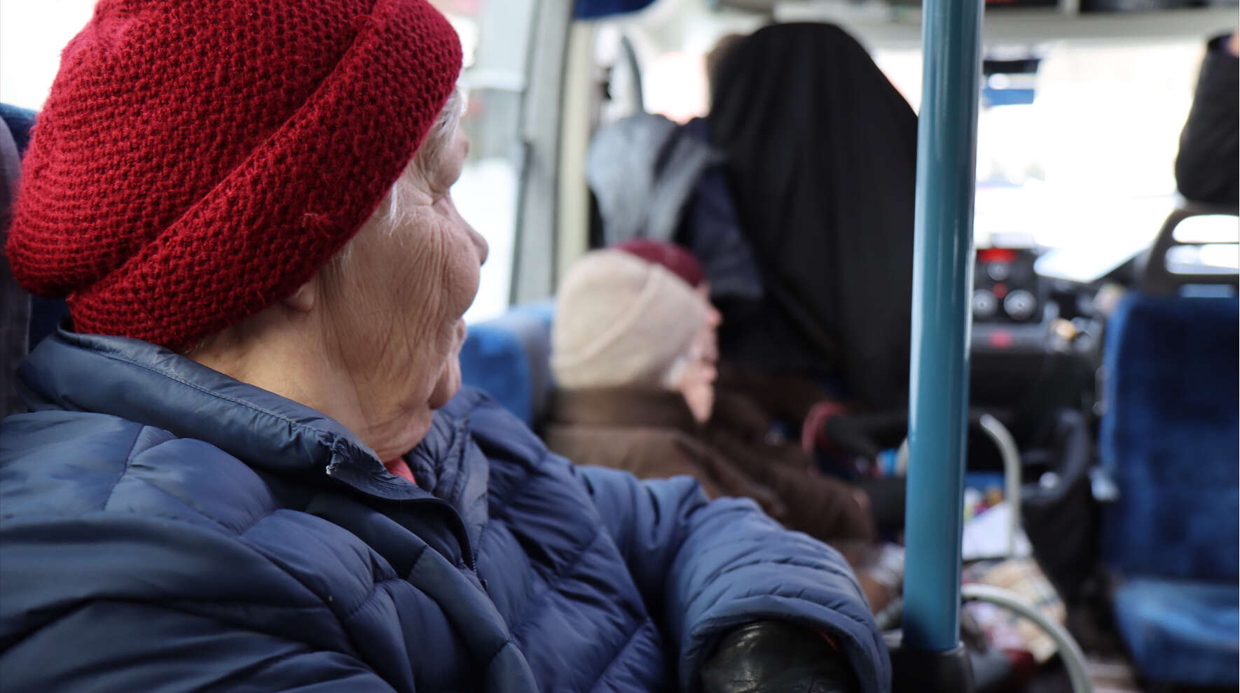 Ikääntynyt istuu bussin penkillä, ja taustalla näkyy muita matkustajia.