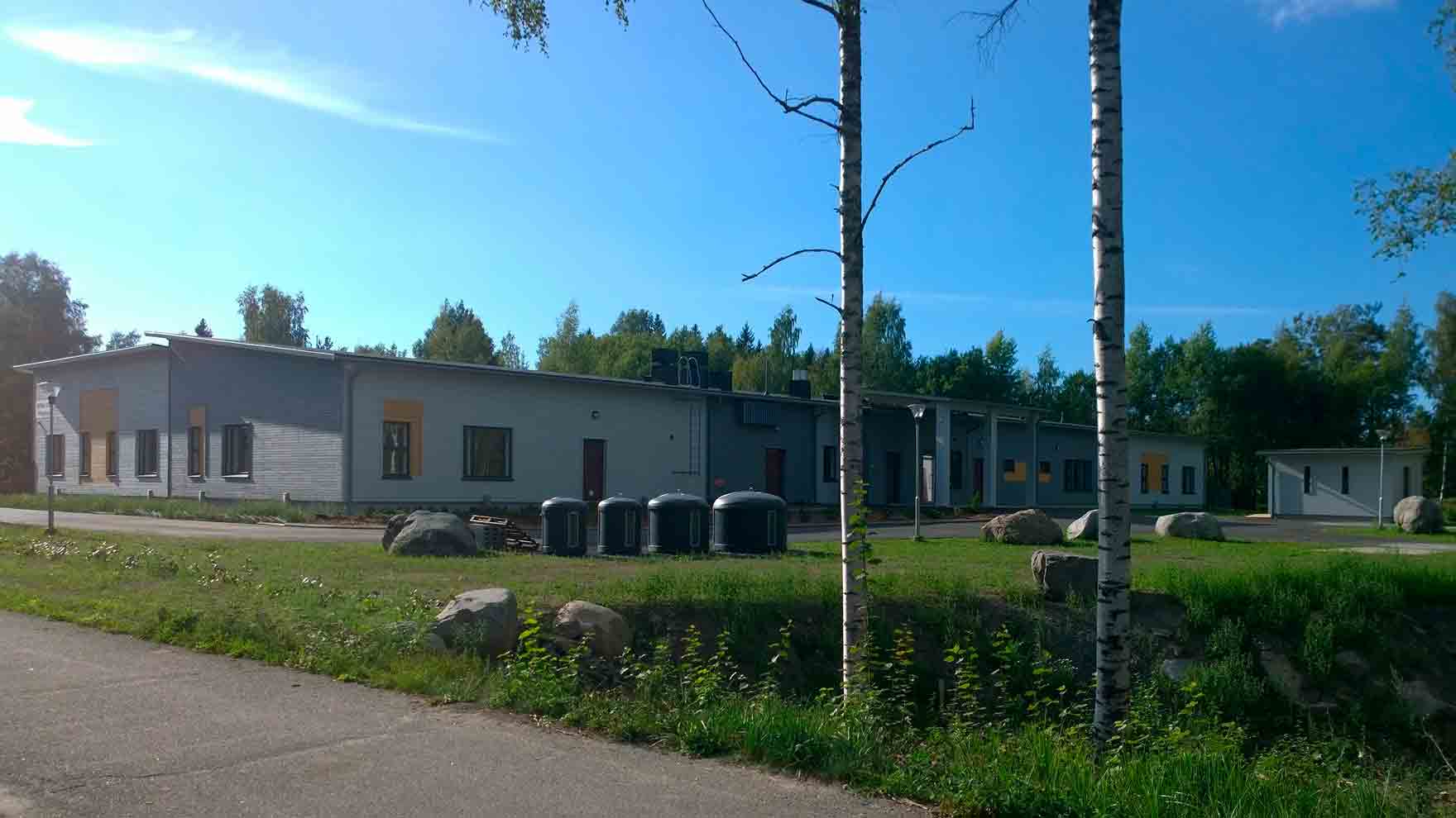 Vaalea matala rakennus, jonka vieressä iso nurmikenttä ja koivuja