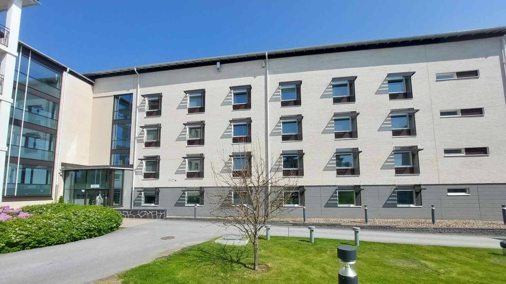 Kerrostaloa muistuttava rakennus, jonka pihassa istutuksia