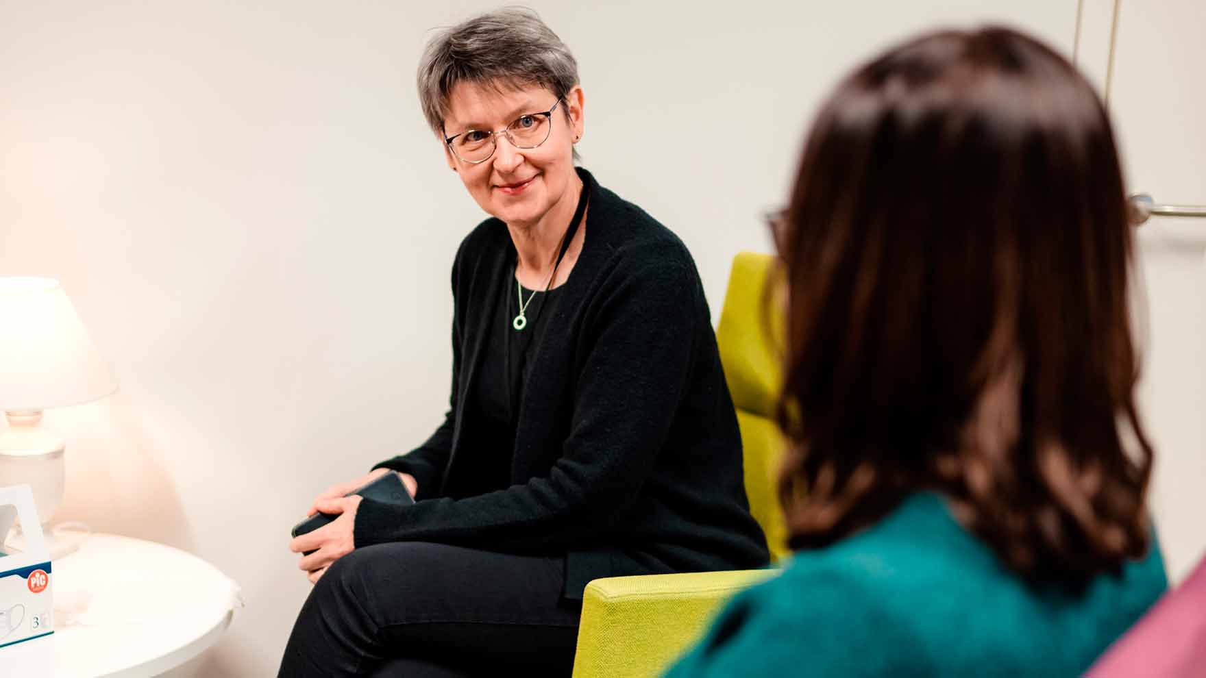 Ammattilainen katsoo hymyillen hänen vieressään istuvaan asiakkaaseen.