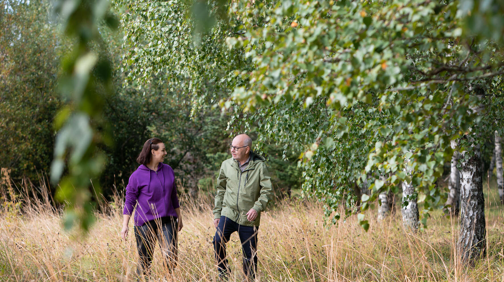 Mies ja nainen kävelevät niityllä metsän reunassa.