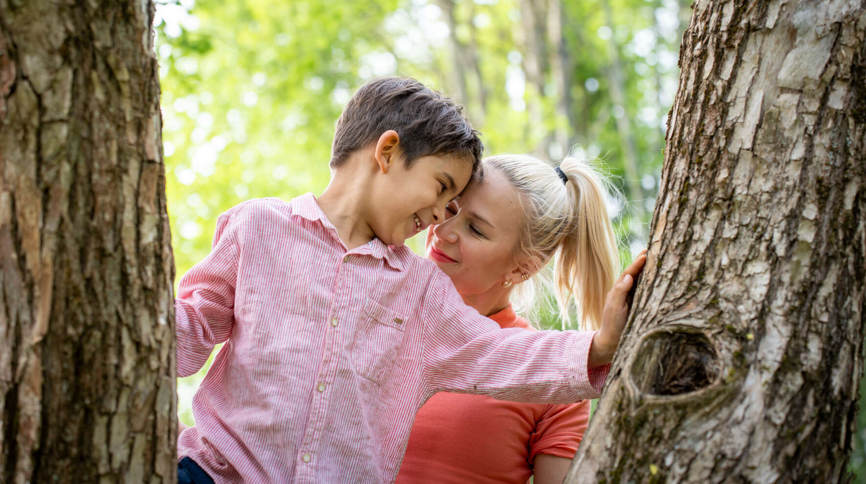 Poika kiipeilee puussa ja aikuinen on lähellä hänen tukenaan.