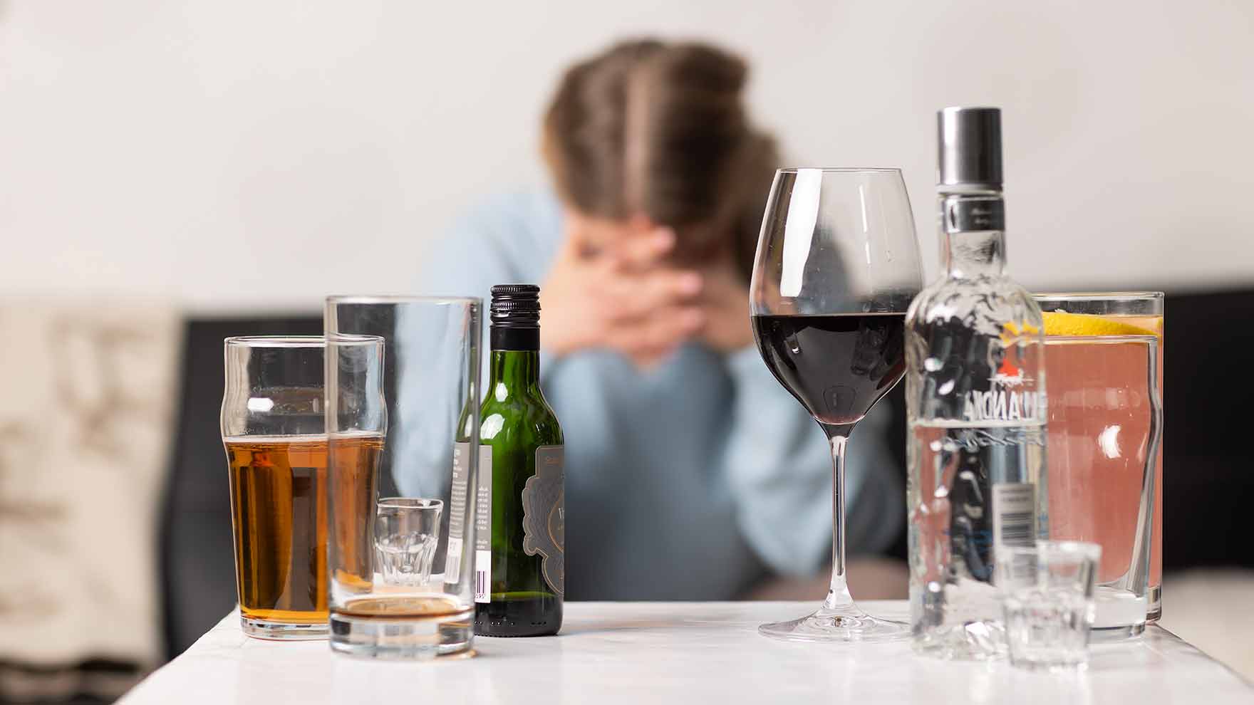 nainen istuu sohvalla ja hänellä on paha mieli liittyen alkoholin käyttöön. Pöydällä alkoholijuomia.