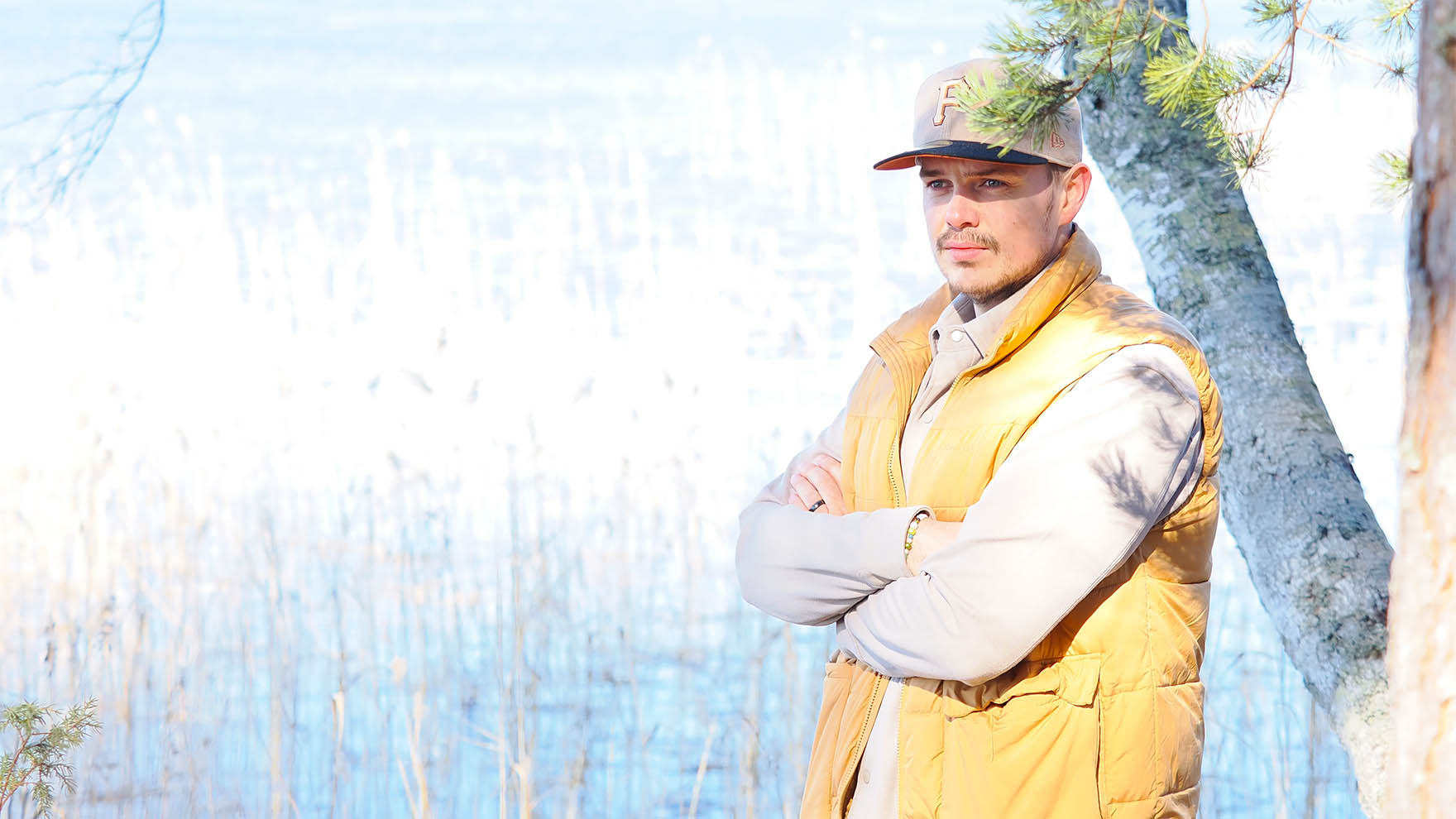 Nuori mies seisoo mietteliään näköisenä puun varjossa järven rannalla.