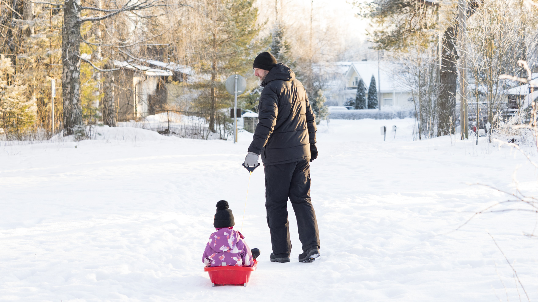 Mies vetää lasta pulkassa talvisessa maisemassa.
