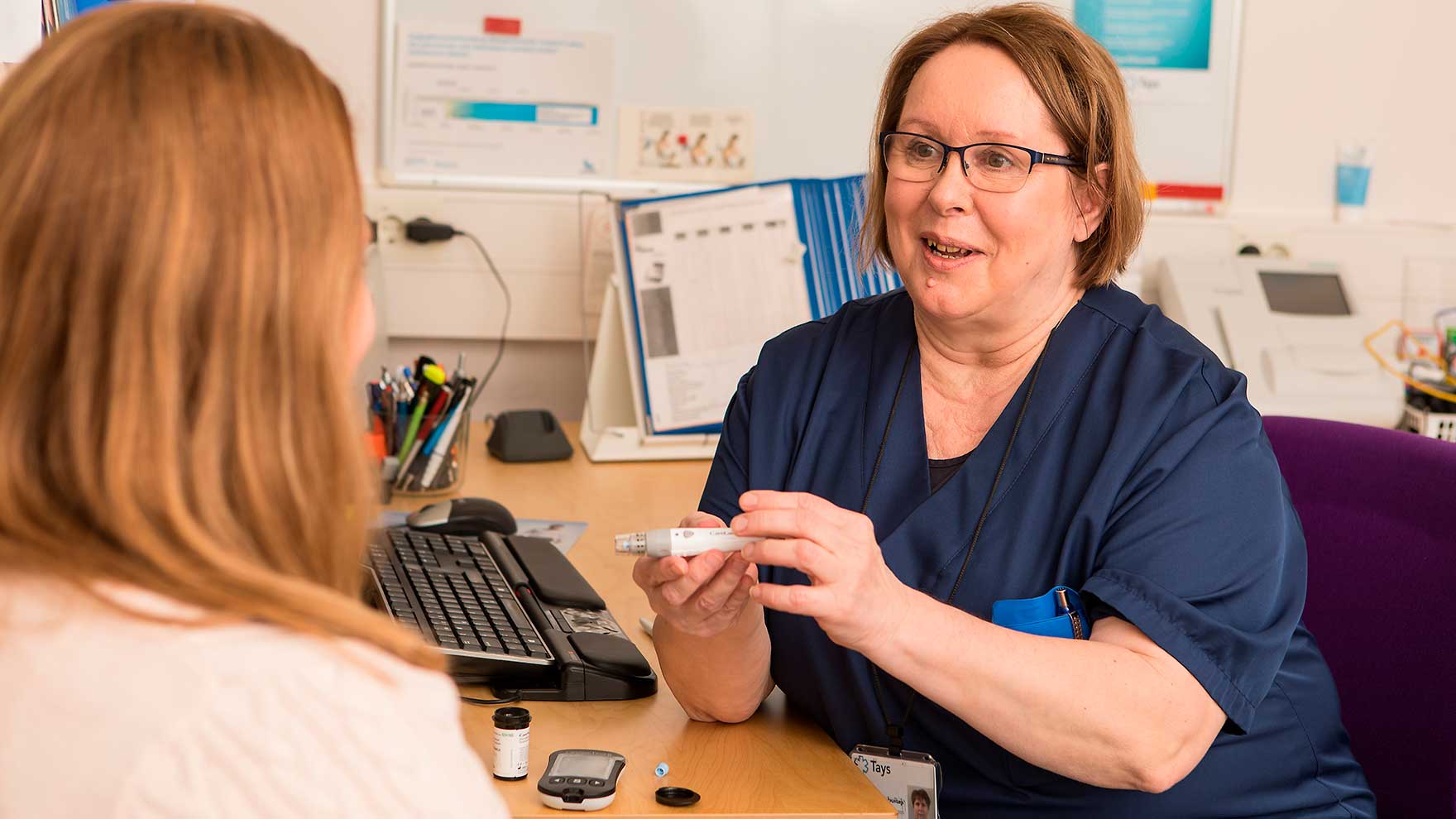 Terveydenhuollon ammattilainen esittelee asiakkaalle verensokerimittaria.